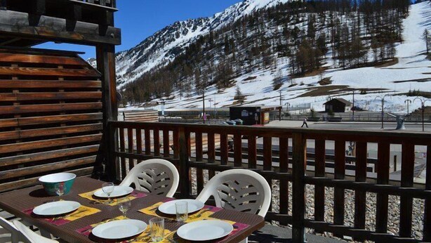 A dining table set outdoors with chairs, a wooden deck, and a mountainous backdrop. - 10m from resort center, 1st floor, view ski slopes, terrace, tv, ski locker, 30m², Montgenèvre (Montgenèvre)