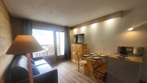 Une pièce de taille modeste comprenant un canapé, une table à manger avec des chaises, un petit coin cuisine et un téléviseur fixé au mur.
