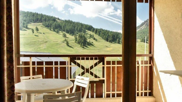 Un balcon donnant sur une colline verdoyante, avec des balustrades en bois et une table ronde entourée de chaises.
