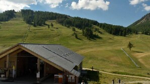 Un bâtiment rustique, doté d’un toit en pente, situé dans un paysage vallonné sous un ciel dégagé.