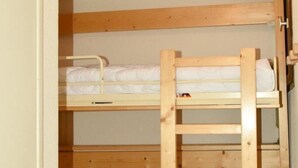 Une chambre avec un lit superposé, une échelle en bois, un luminaire au plafond et une porte.