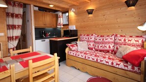 A cozy cabin interior with a wooden dining table, a sofa with patterned cushions, and a kitchen area with wooden cabinets and a black countertop. - 300m from ski slopes, 2nd floor, view panoramic, balcony, tv, ski locker, 45m², Les Saisies (Les Saisies)