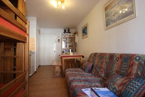 Ett mysigt vardagsrum med en mönstrad soffa, trämöbler och en matplats med ett bord och stolar.