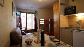 A compact kitchen with a microwave, coffee maker, and a small refrigerator. A dining table with striped cups and a kettle is set up near a window with curtains. - 100m from ski slopes, 2nd floor, balcony, tv, 24m², Val Thorens (Val Thorens)