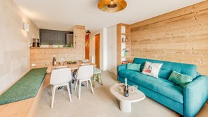 A modern living room with a teal sofa, a dining area with a wooden table, and a kitchen with a wooden wall. - 200m from ski slopes, 3rd floor, balcony, fireplace or stove, tv, ski locker, 54m² (Champagny-en-Vanoise)