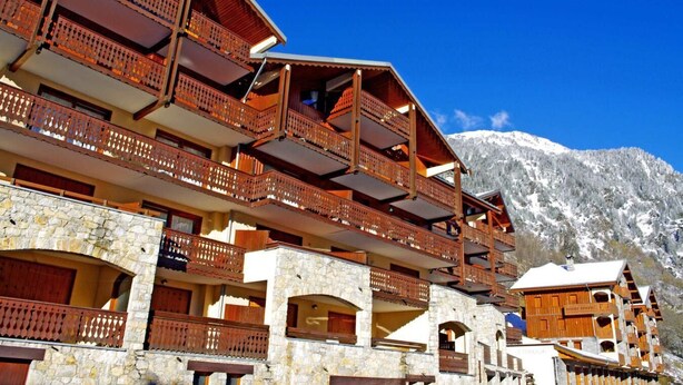 Ein mehrstöckiges Hotel mit hölzernen Balkonen und Steinsäulen vor einer verschneiten Berglandschaft.