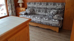 Ein Holzinterieur mit Schlafsofa, kleinem Tisch und Lampe.