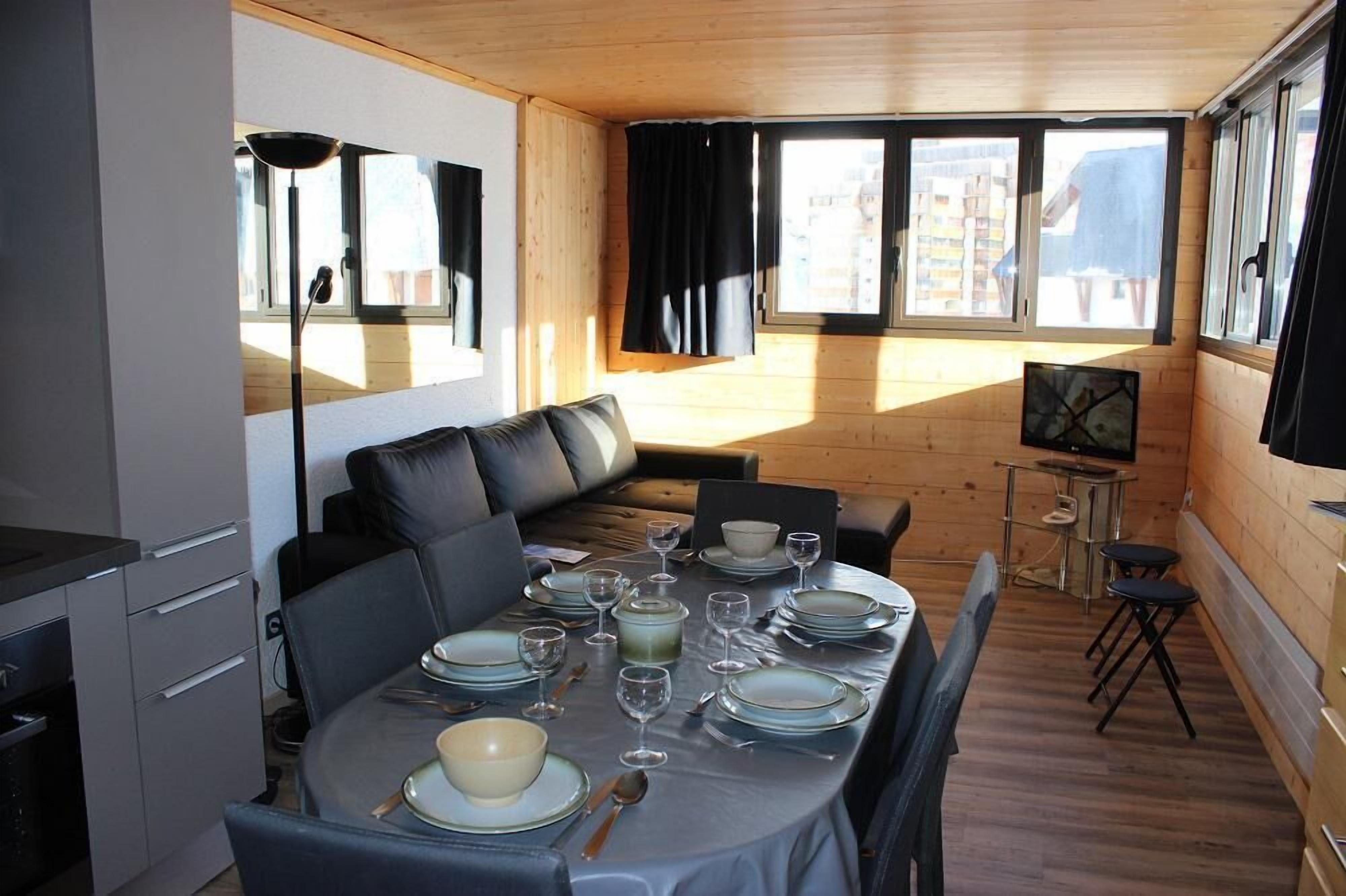 Un coin repas avec une table dressée pour quatre personnes, un canapé et un petit téléviseur posé sur un meuble.