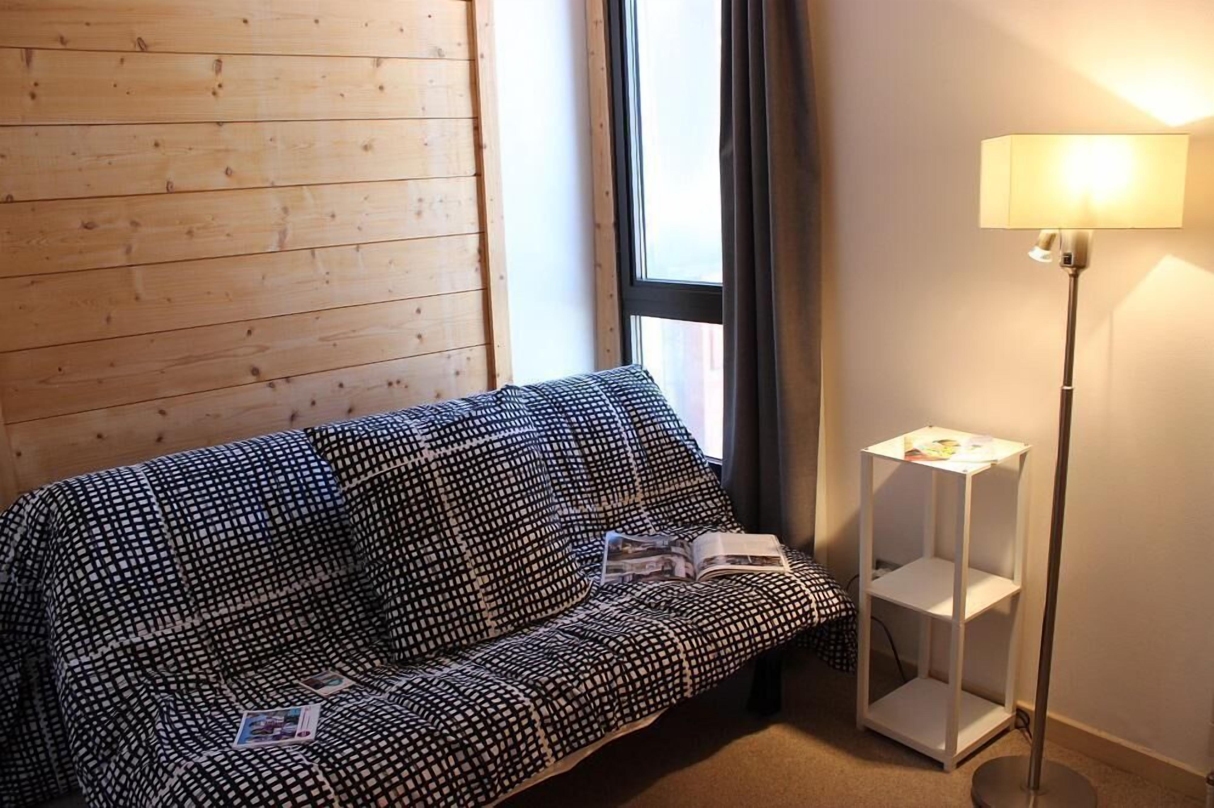 A room with a patterned sofa, a standing lamp, and a window with curtains.