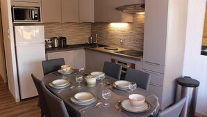 Cozinha compacta equipada com micro-ondas, frigorífico e mesa de jantar para quatro pessoas, posta com pratos, copos e talheres.
