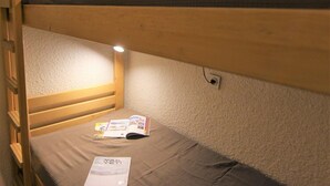Uma cama beliche com um colchão simples, um livro e um abajur.