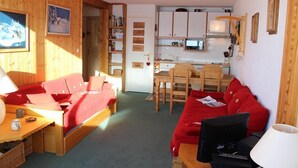 A cozy room with a red sofa, a wooden dining table, and a kitchen area with white cabinets and a microwave.