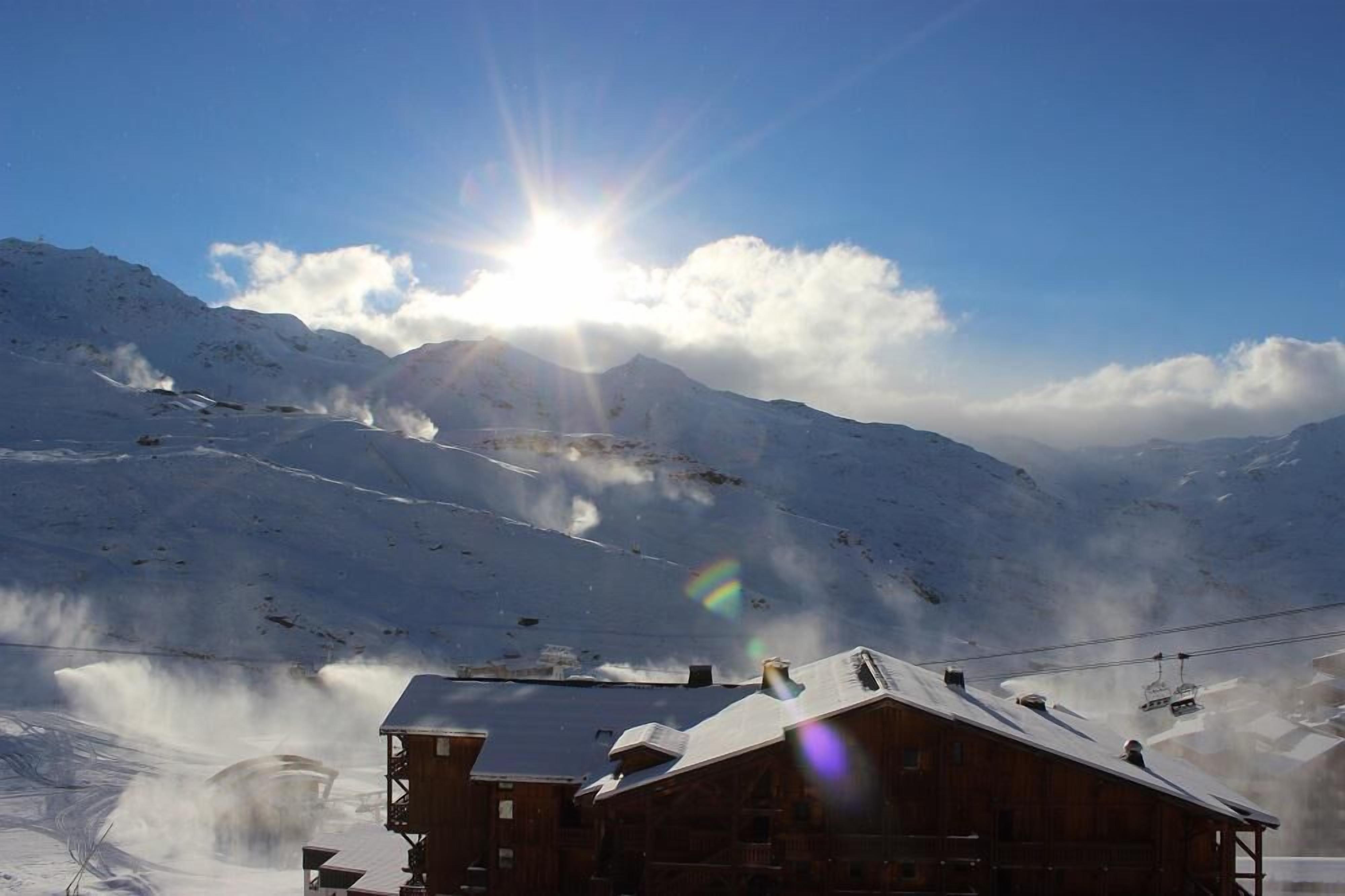 A wooden mountain lodge with a snow-covered roof, surrounded by snow-covered mountains and a clear sky.