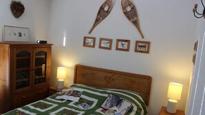 A bedroom with a wooden headboard, a green quilt with photos, a wooden cabinet, and wall-mounted picture frames.