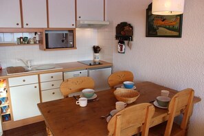 Een kleine keuken met witte kastjes, een magnetron en een eettafel met stoelen.