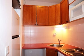 A compact kitchen with wooden cabinets, a built-in microwave, a sink, and a stove.