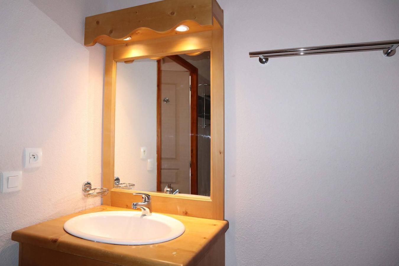 Een badkamer met een houten wastafel, een witte wasbak, een spiegel en een handdoekhouder.