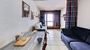 A living room with a sofa, a dining table with a pitcher and bowl, and a window with curtains. - 10m from ski slopes, 10th floor, view ski slopes, swimming pool, balcony, tv, ski locker, 22m² (Le Corbier)
