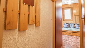 Ein Flur mit an der Wand befestigten Holz-Haken, einer Tür zu einem Zimmer mit Bett und Fenster sowie einem Deckenventilator.
