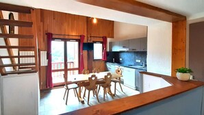 Une cuisine avec des meubles en bois, un coin repas avec une table et des chaises, et une vue sur l’extérieur.
