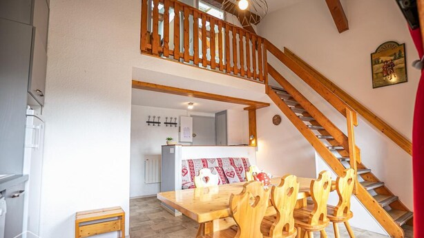 Un coin repas avec une table et des chaises en bois, un petit tabouret en bois et un escalier avec des rampes en bois.