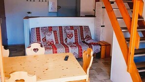Un coin repas avec une table et des chaises en bois, un canapé agrémenté de coussins à motifs et un escalier avec des rampes en bois.