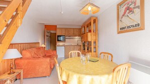 A cozy room with a wooden staircase, a sofa, a dining table with chairs, a kitchen area, and a framed poster on the wall. - 150m from resort center, 2nd floor, balcony, tv, ski locker, 29m², Aussois (Aussois)