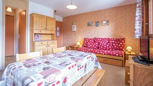 A cozy bedroom with a bed, a wooden wardrobe, a desk with a computer, and a red patterned sofa. - 10m from ski slopes, 1st floor, balcony, tv, 26m², Aussois (Aussois)