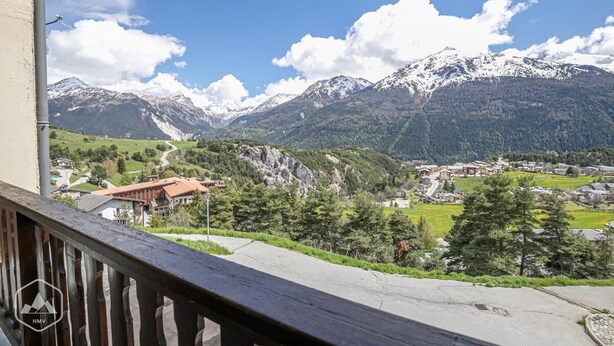 A mountain landscape with snow-capped peaks, a village below, and a wooden balcony railing. - 10m from ski slopes, 1st floor, balcony, tv, 26m², Aussois (Aussois)