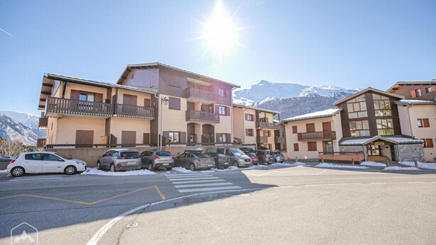 A multi-story building with balconies, a parking lot, and snow-covered mountains in the background. - 350m from resort center, 1st floor, terrace, tv, 30m², Aussois (Aussois)