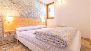 A bedroom with a stone wall, wooden headboard, and a bed with a floral comforter. - 350m from resort center, 1st floor, terrace, tv, 30m², Aussois (Aussois)