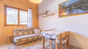 A cozy room with a wooden sofa, a dining table with chairs, a window with curtains, and a wall-mounted shelf with a decorative item. - 350m from resort center, 1st floor, terrace, tv, 30m², Aussois (Aussois)