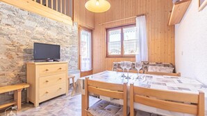 A cozy room with a stone wall, wooden furniture, a television, and a dining table with glasses. - 350m from resort center, 1st floor, terrace, tv, 30m², Aussois (Aussois)