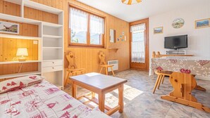 Une pièce chaleureuse aux murs en bois, avec un lit recouvert d’une couverture à motifs, un bureau avec une télévision et une fenêtre donnant sur l’extérieur.