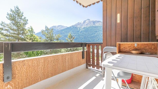 Un balcon avec vue sur les montagnes, un mur en bois et une table avec des chaises.