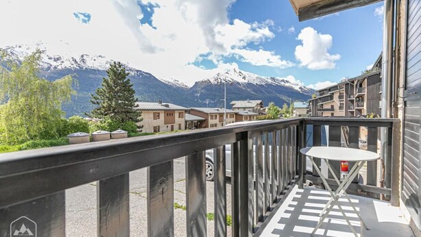 En balkon med udsigt til sneklædte bjerge, et lille bord og et gelænder.