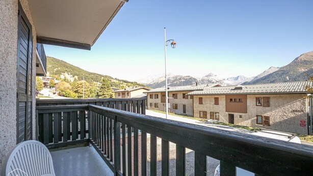 Ein Balkon mit Blick auf ein Gebirge, eine Fahnenstange und ein Gebäude mit zahlreichen Fenstern.