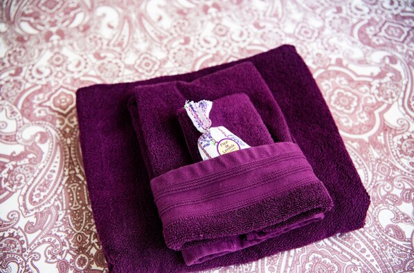 Ein gefaltetes violettes Handtuch mit einem lavendelfarbenen Anhänger vor einem gemusterten Stoffhintergrund.