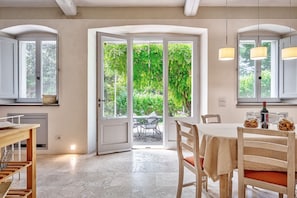 Un coin repas avec une table et des chaises, une cuisine équipée d’armoires et une grande porte vitrée donnant sur un jardin.