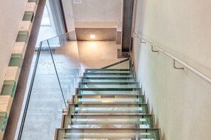 A modern interior with a glass staircase, a concrete floor, and a light fixture on the ceiling.