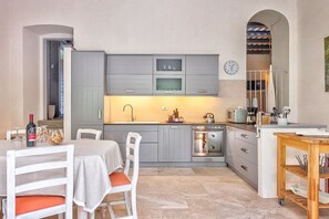 Eine kleine Küche mit grauen Schränken, einer Mikrowelle, einem Backofen und einem Essbereich mit Tisch und Stühlen.