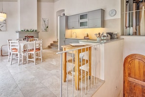 A modern kitchen with grey cabinets, a wooden dining table with white chairs, and a staircase with a railing.