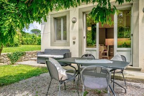Een terras met een tafel en stoelen, een stenen muur en uitzicht op het interieur door een glazen deur.