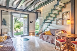 A modern interior with a staircase, a sofa, a table, and a glass door leading to a garden.