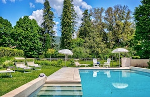A swimming pool with lounge chairs and umbrellas, surrounded by greenery and trees.