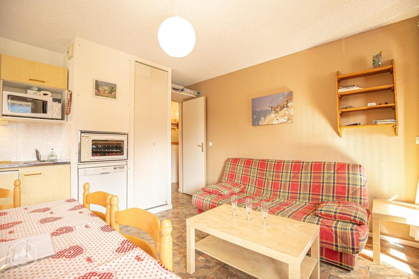 Een gezellige woonkamer met een geruite bank, een houten tafel en een keukenhoek met een magnetron en oven.