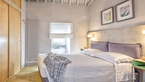 Ein Schlafzimmer mit Bett, Nachttischen, Heizkörper, Fenster und gerahmten Kunstwerken an der Wand.