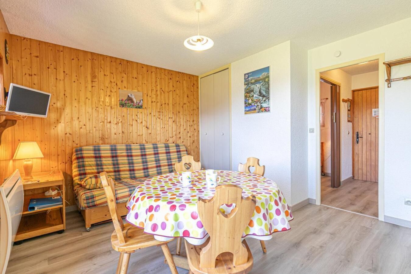 Een gezellige kamer met een houten wand, een bank, een tafel met een stippen tafelkleed en een televisie op een standaard.