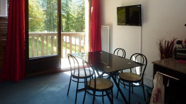 A dining area with a glass table and four chairs, a television on the wall, and a view of a deck and trees outside. - 300m from ski slopes, 2nd floor, view forest, balcony, tv, ski locker, 24m², Les Orres (Les Orres)