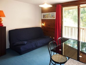 A room with a dark blue sofa, a small round table with a chair, a lamp, and a painting on the wall.
